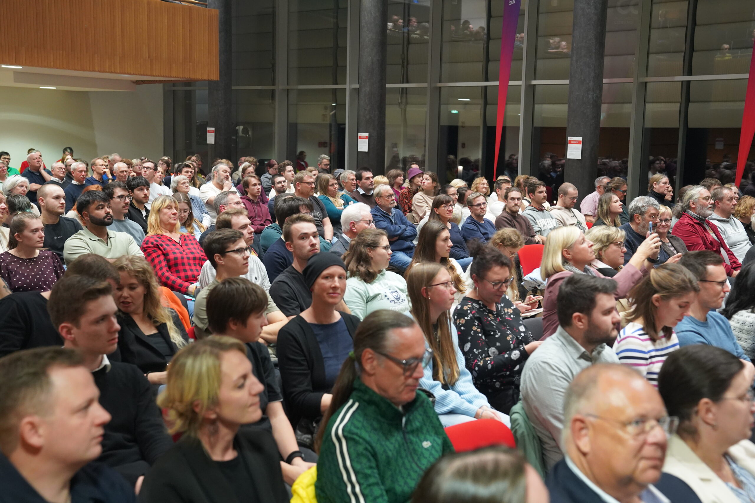 Ein großes, vielfältiges Publikum verfolgt von den Stuhlreihen in einem modernen, glasverglasten Gebäude aus eine automatisierte Präsentation. at Hochschule Coburg