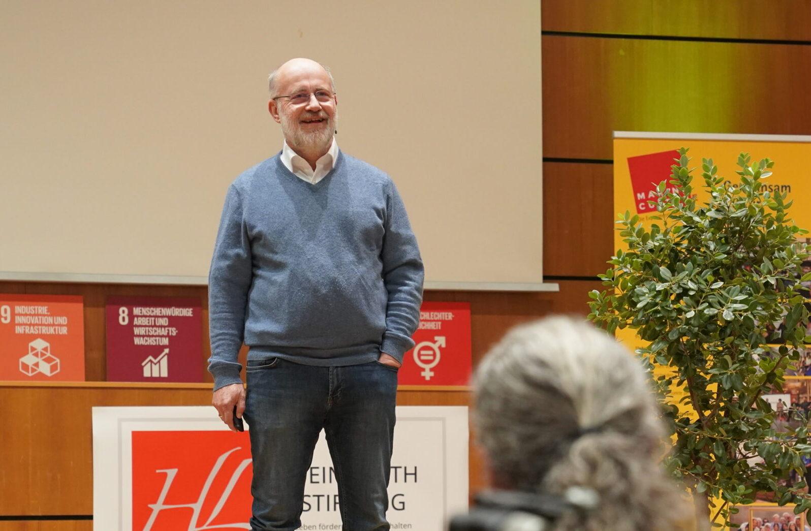 Ein Mann in einem blauen Pullover und Jeans steht auf einer Bühne und spricht vor Publikum über automatisiertes Design. at Hochschule Coburg