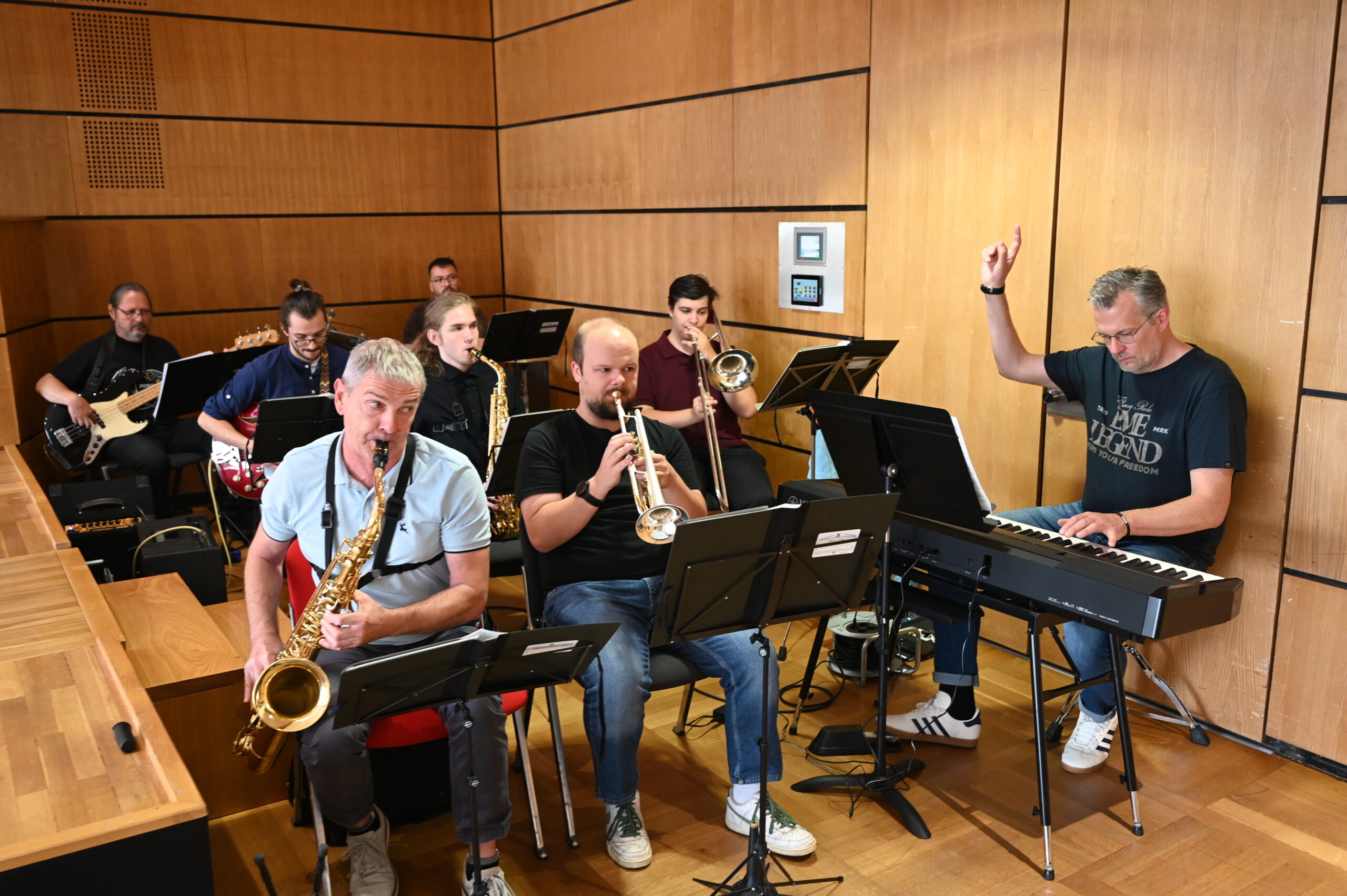 Ein siebköpfiges Jazzensemble probt in einem holzgetäfelten Raum an der Hochschule Coburg; im Vordergrund stehen ein Saxophonist, ein Trompeter und ein Keyboarder, die übrigen Musiker befinden sich im Hintergrund. at Hochschule Coburg