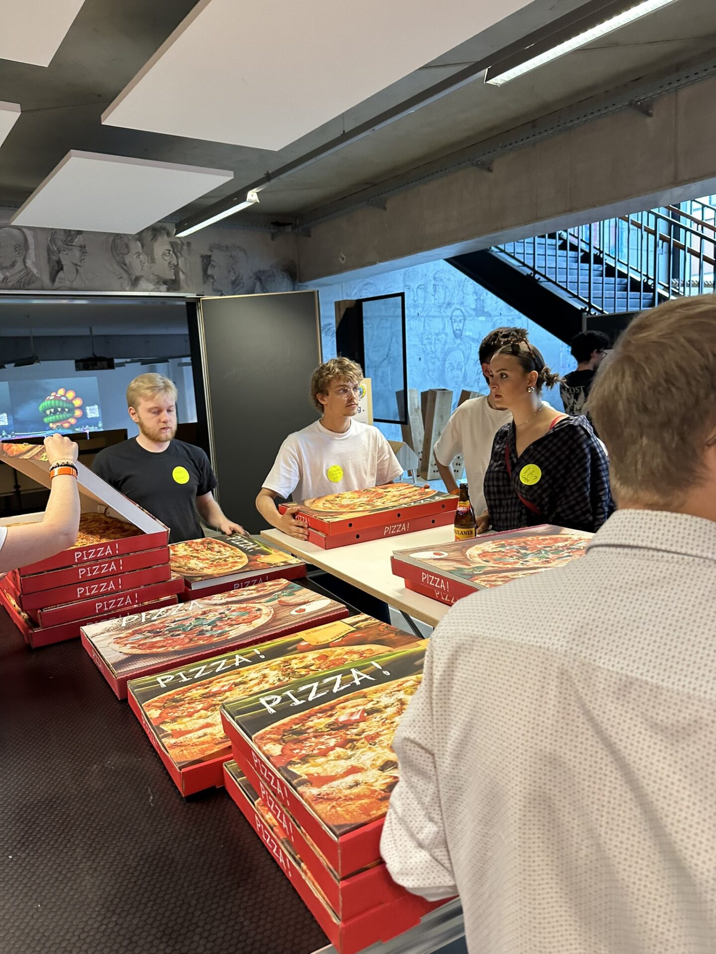Eine Gruppe junger Erwachsener steht an der Hochschule Coburg um einen langen Tisch herum, auf dem Stapel von Pizzakartons liegen. at Hochschule Coburg