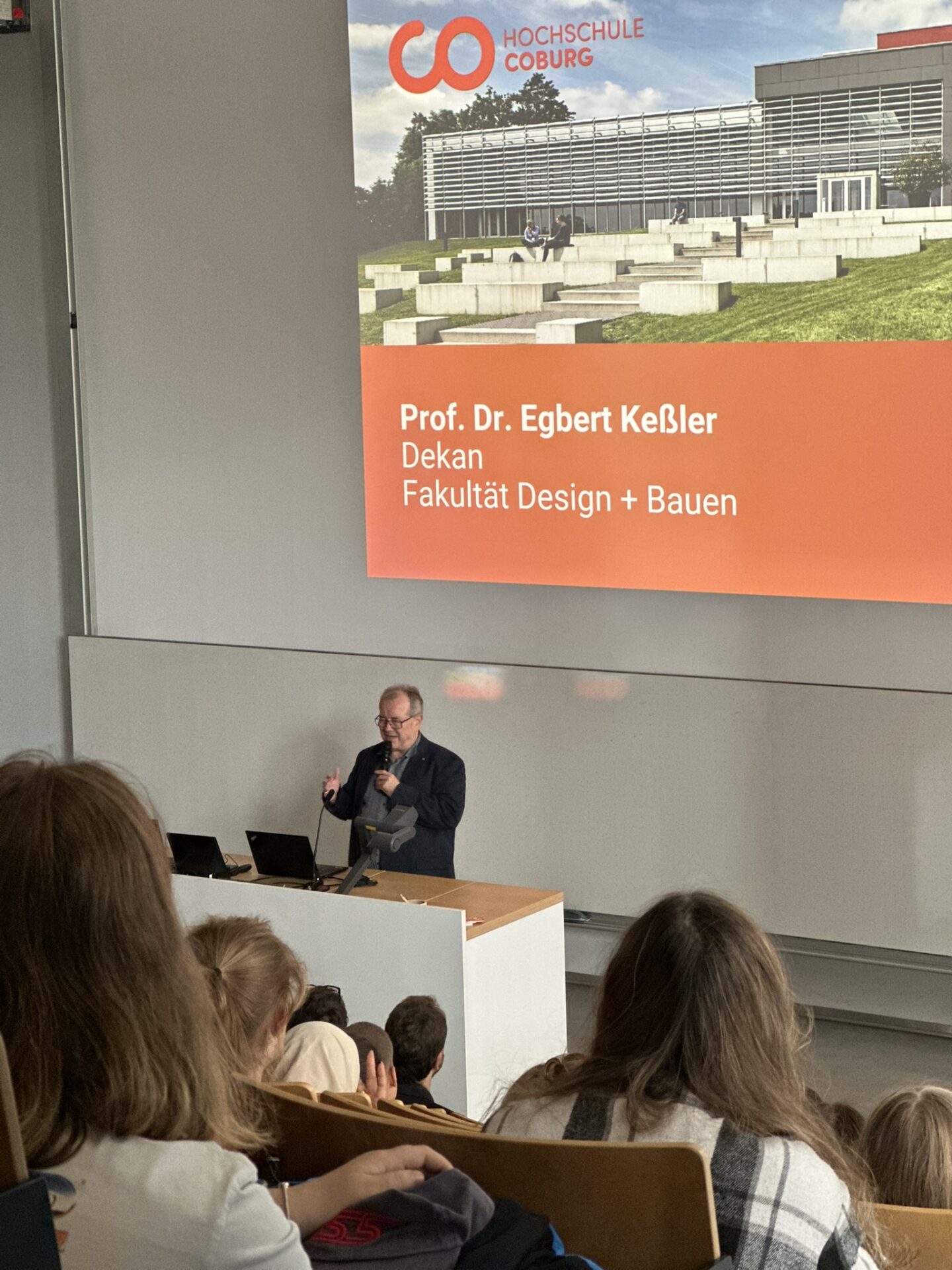 Dekan Professor Dr. Egbert Keßler steht auf einem Podium in einem Hörsaal der Hochschule Coburg vor einer Leinwand, auf der sein Name, sein Titel und das Logo der Hochschule zu sehen sind. at Hochschule Coburg