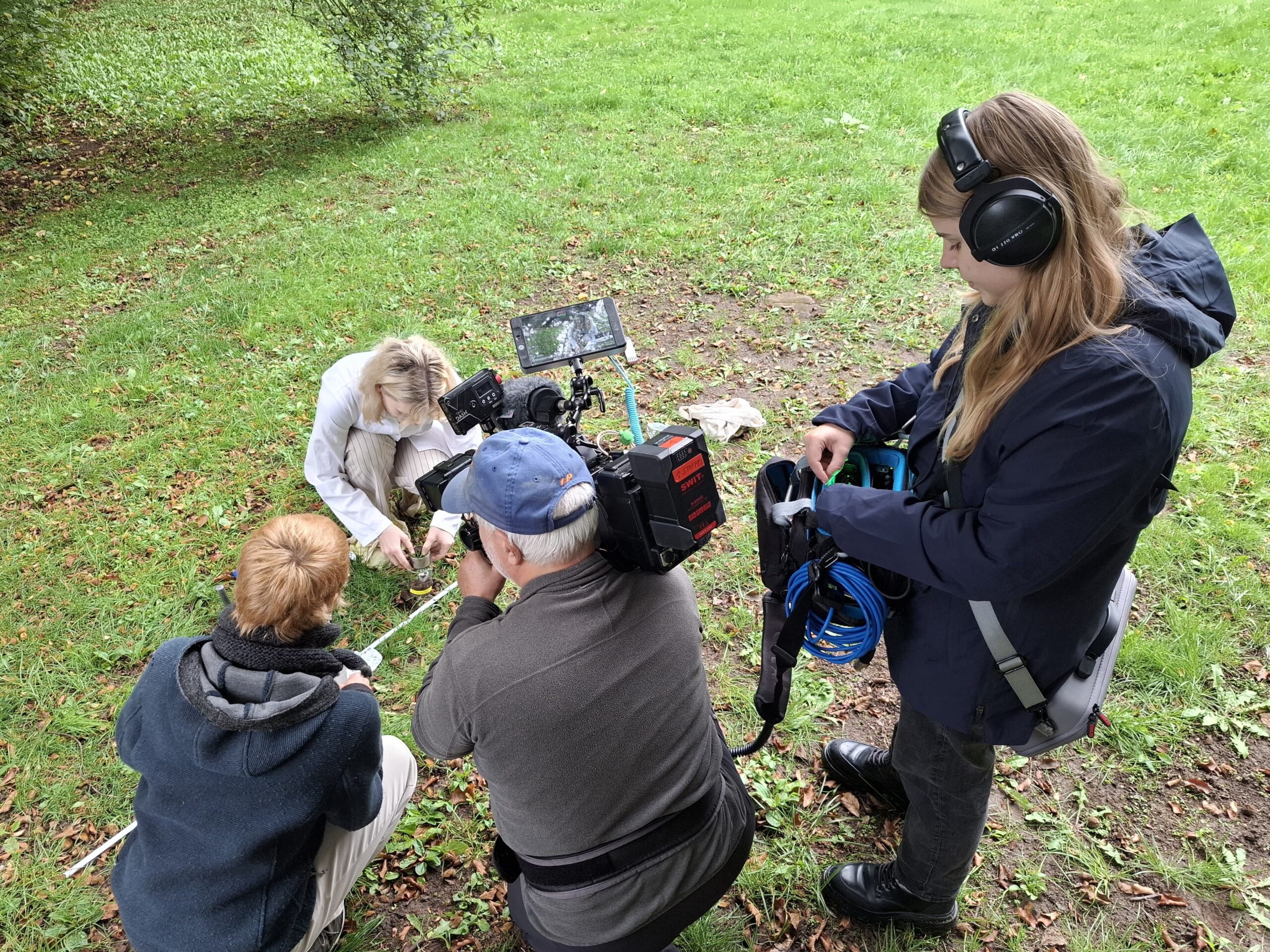 Ein Filmteam nimmt eine spontane Aufnahme einer Frau auf, die auf einer Wiese hockt. at Hochschule Coburg