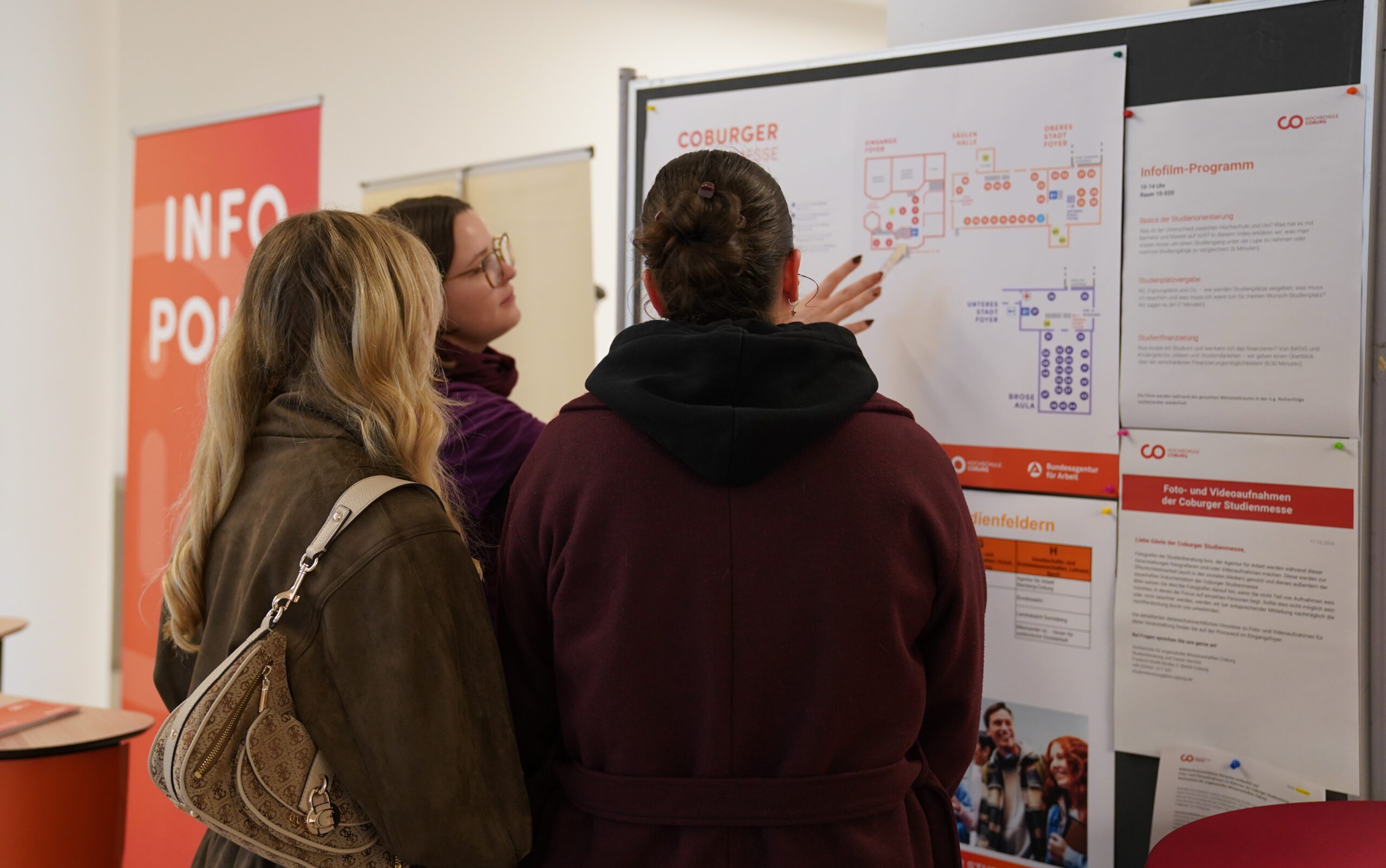Drei Personen schauen sich einen Veranstaltungsplan der Universität Coburg an, um sich auf der Studienmesse zurechtzufinden und ihre Studienwahl zu treffen. at Hochschule Coburg