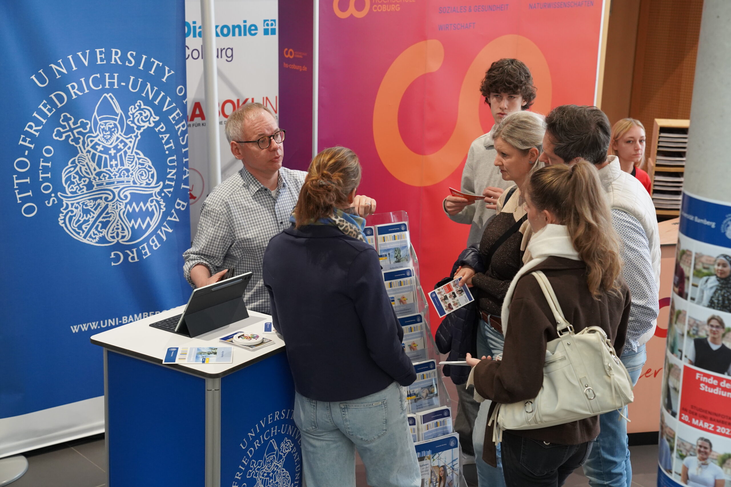 Ein Vertreter der Universität bietet einer Gruppe von Studieninteressierten am Informationsstand der Coburger Studienmesse Studienberatung an. at Hochschule Coburg