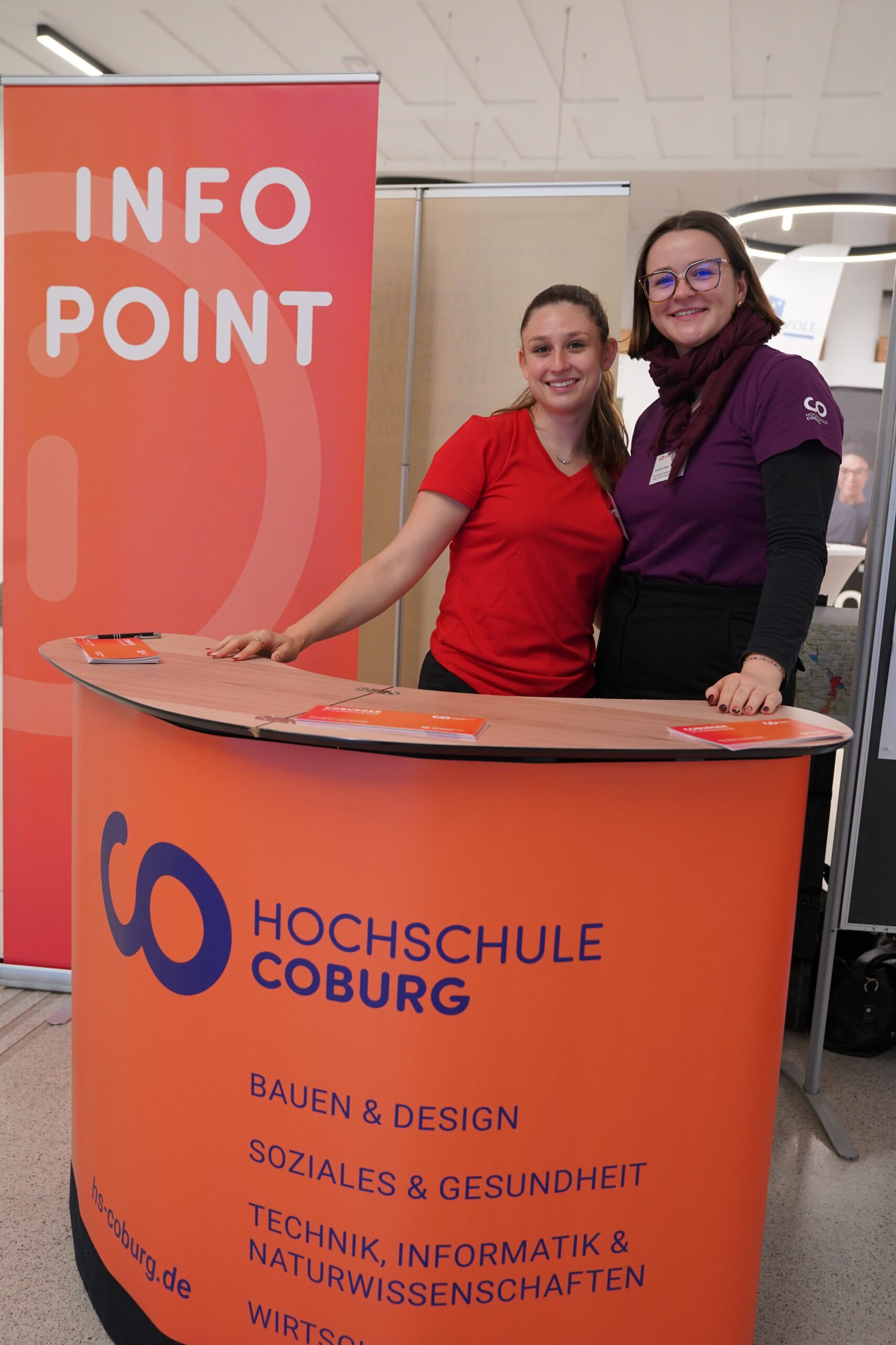 Hinter einem orangefarbenen Infotisch der Hochschule Coburg stehen zwei Frauen, die Studienberatung anbieten. at Hochschule Coburg