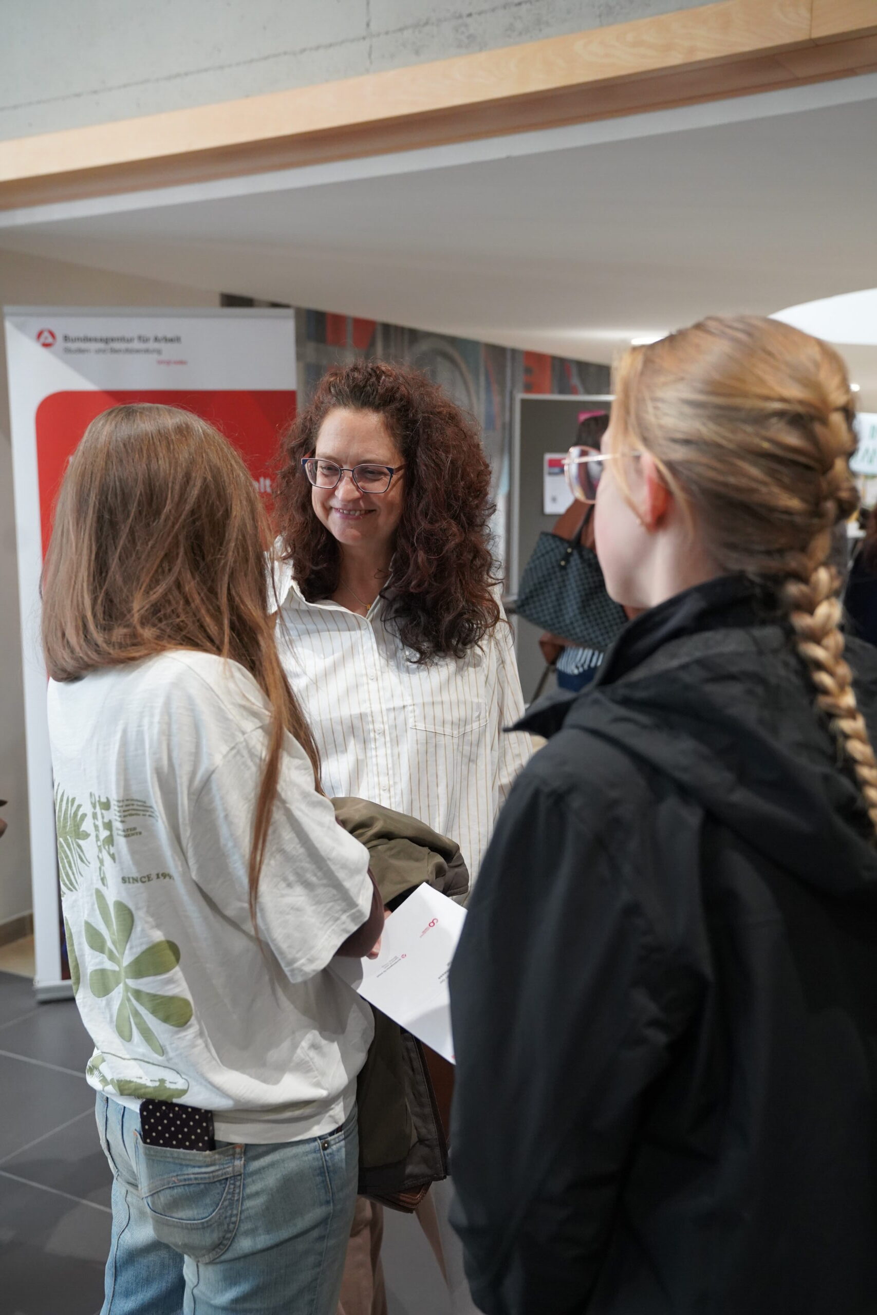 Eine Frau mit lockigem Haar, die in einem Bürogebäude zwei junge Menschen bei der Studienberatung unterstützt. at Hochschule Coburg