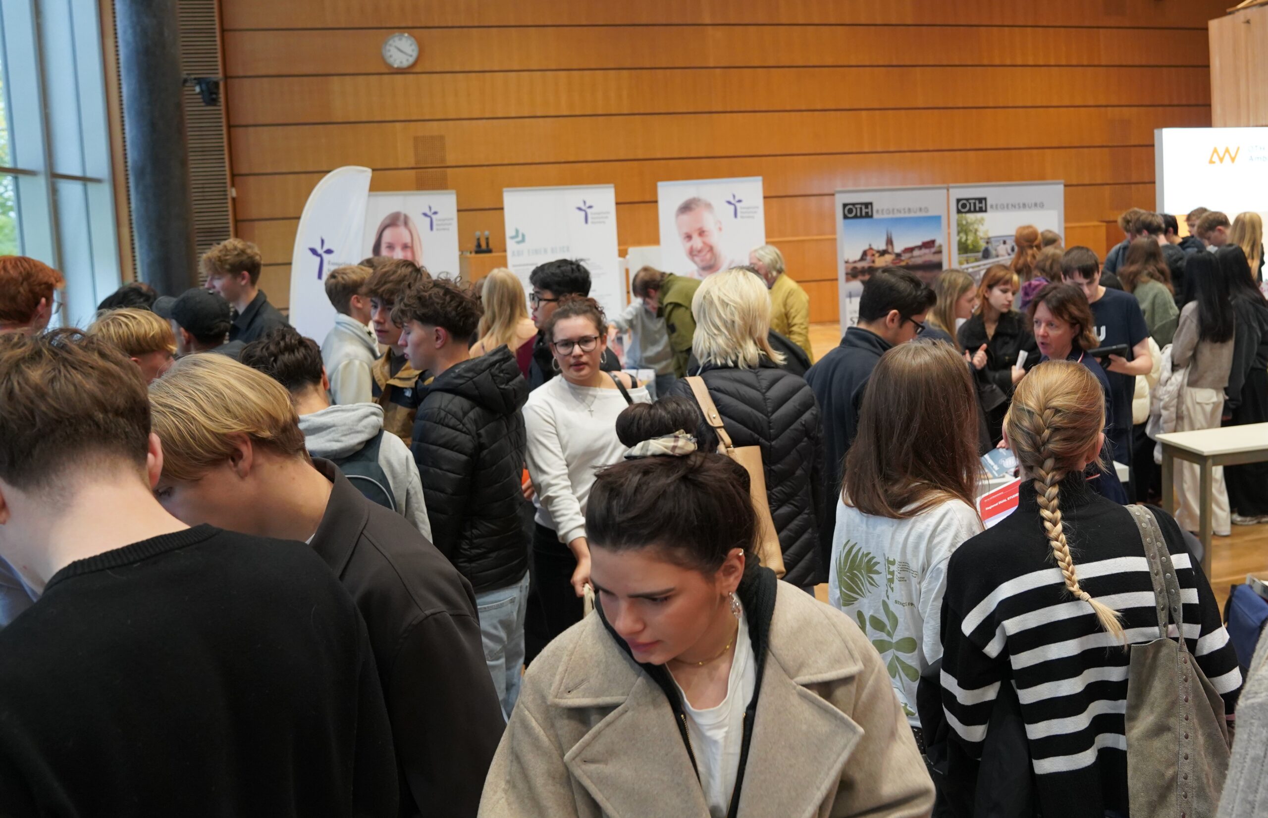 Auf einer gut besuchten Studienmesse in den Räumlichkeiten der Universität schlendern Studierende zwischen Informationsständen mit OTH-Regensburg-Bannern umher und informieren sich über ihre Möglichkeiten bei der Studienwahl. at Hochschule Coburg