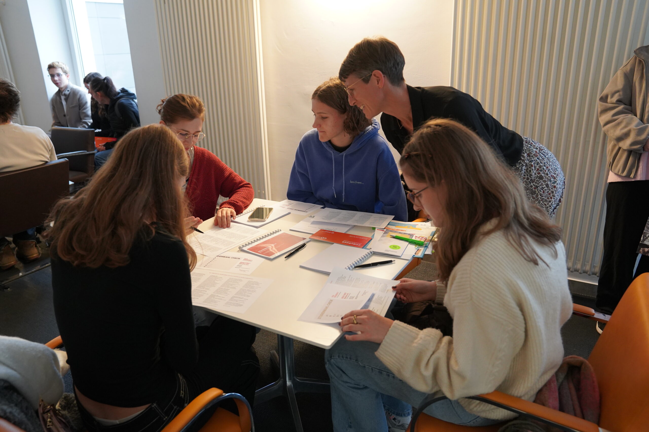 Fünf Personen sitzen bei einem Beratungsgespräch um einen Tisch herum, sehen sich Unterlagen an und machen sich Notizen. at Hochschule Coburg
