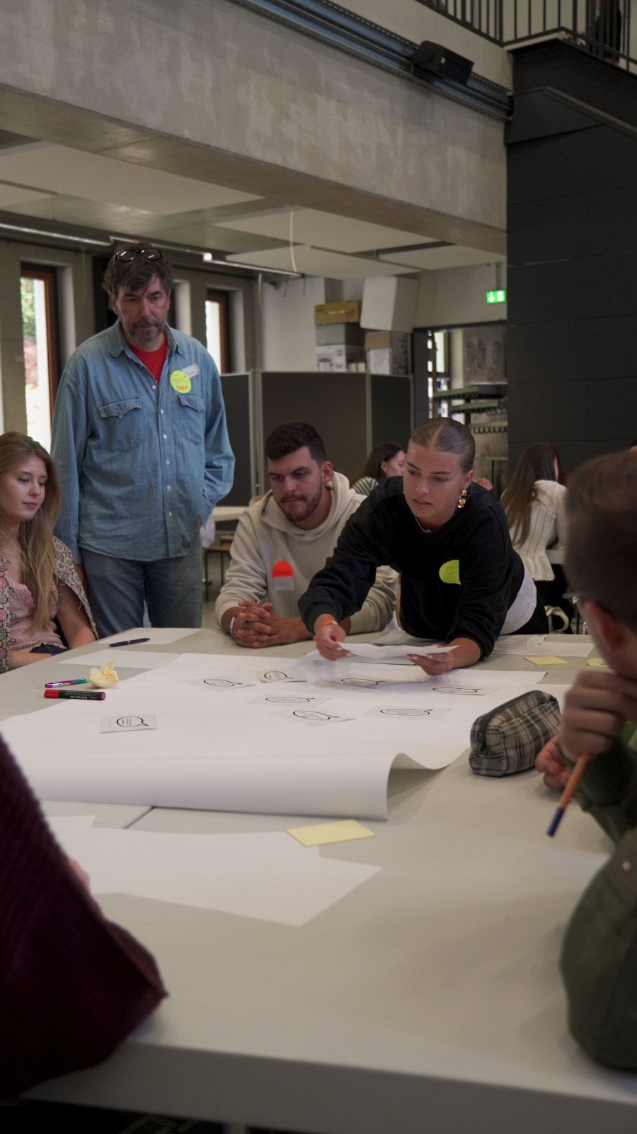 Studierende im ersten Jahr an der Fakultät für Design + Bauwesen arbeiten gemeinsam an einem großen Tisch mit Papieren und Haftnotizen. at Hochschule Coburg
