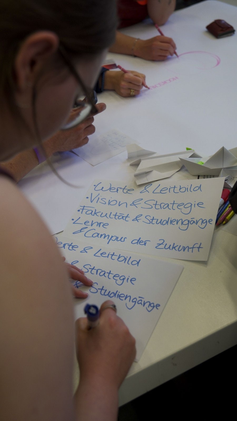 Ein Student schreibt während des „anCOmmen 2026“-Workshops der Fakultät Design + Bauen deutsche Überschriften wie „Werte & Leitbild“ und „Campus der Zukunft“ auf Zettel. at Hochschule Coburg