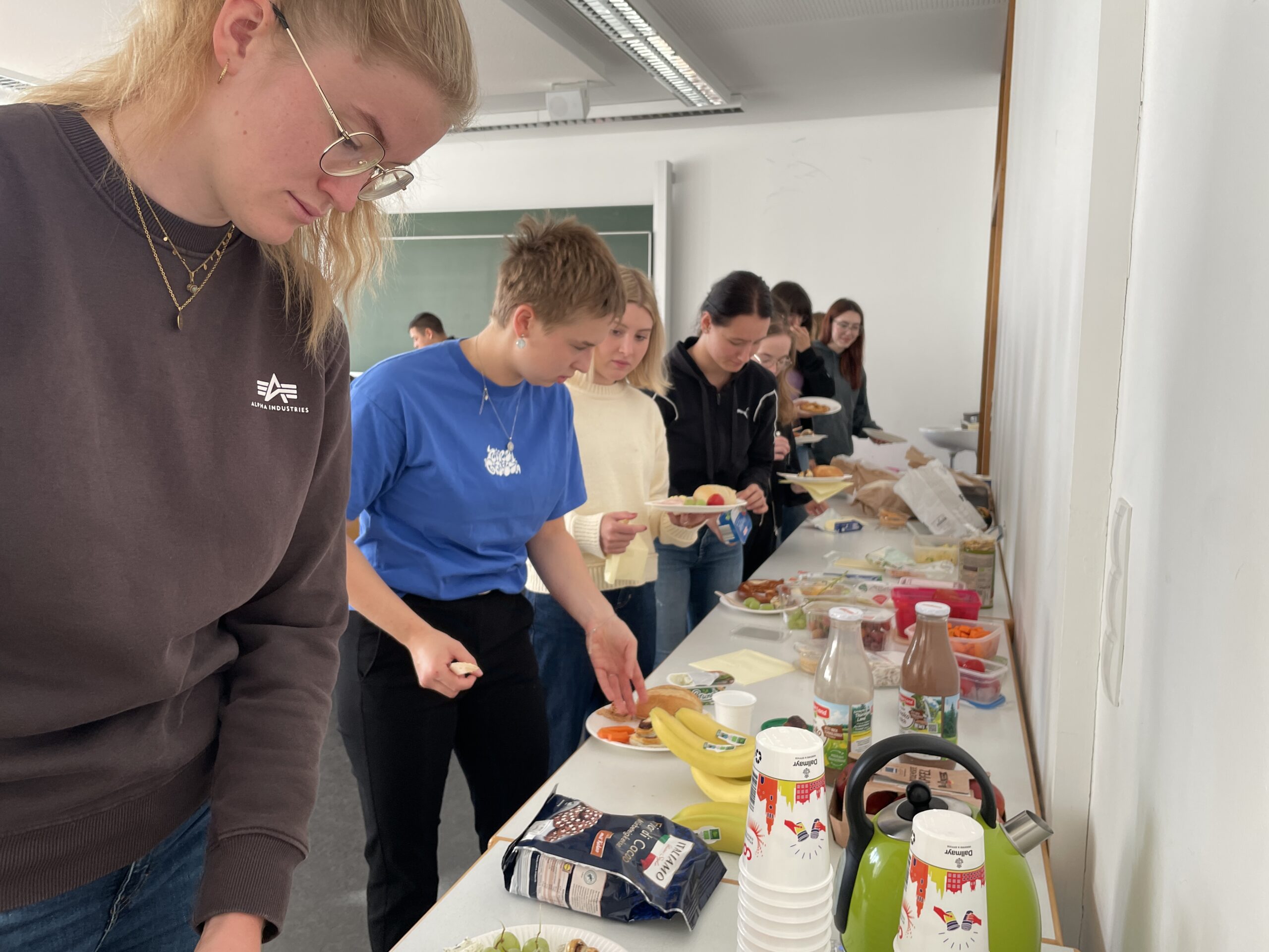 Eine Reihe von MINT-Studierenden, die sich an einem Buffettisch, der in einem Raum für ihren Studienanfang aufgestellt wurde, Essen nehmen. at Hochschule Coburg