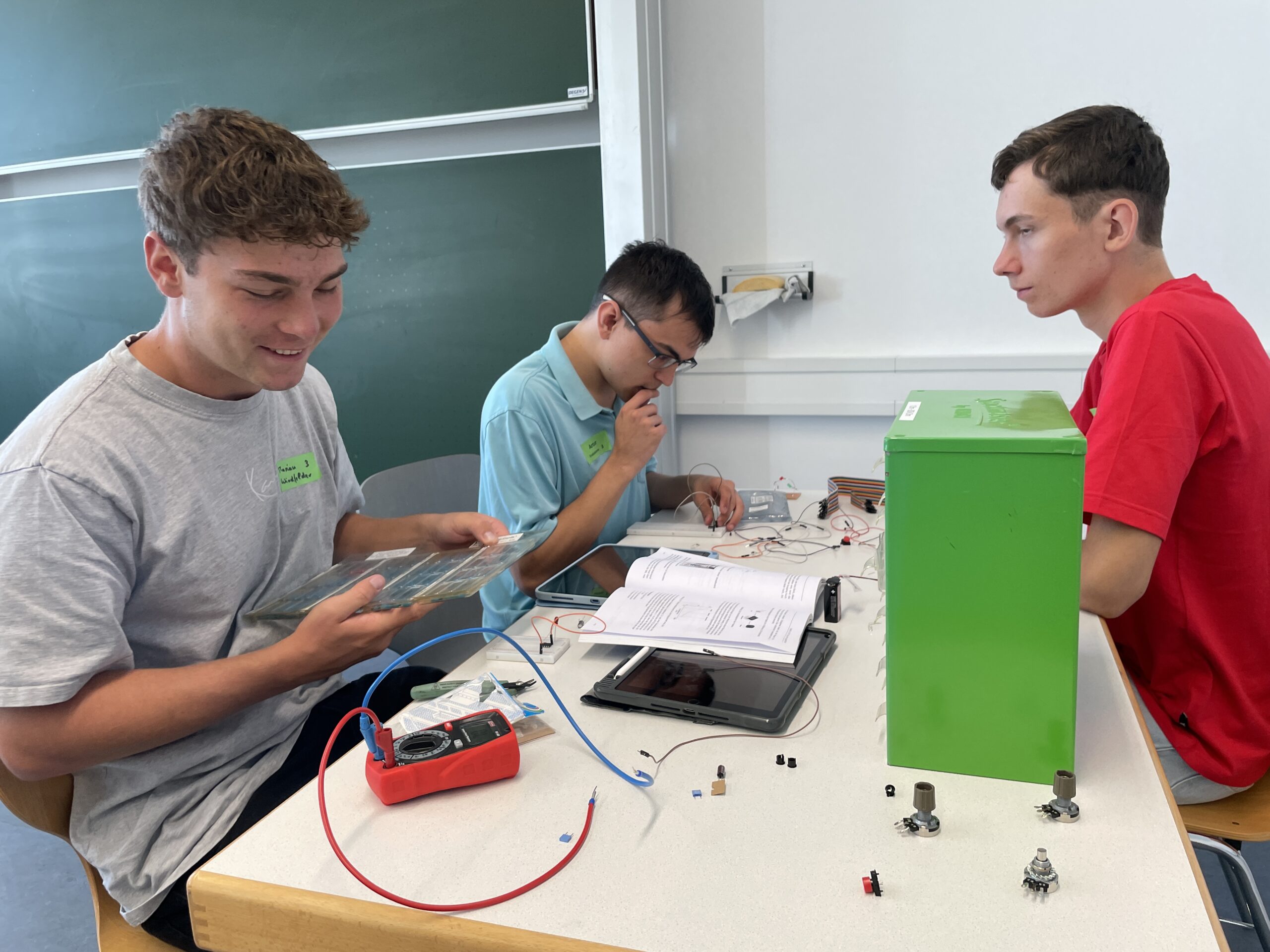 Drei Studierende im ersten Semester arbeiten an einem MINT-Elektronikprojekt an einem Tisch, auf dem ein Multimeter, eine Bedienungsanleitung und Bauteile liegen. at Hochschule Coburg