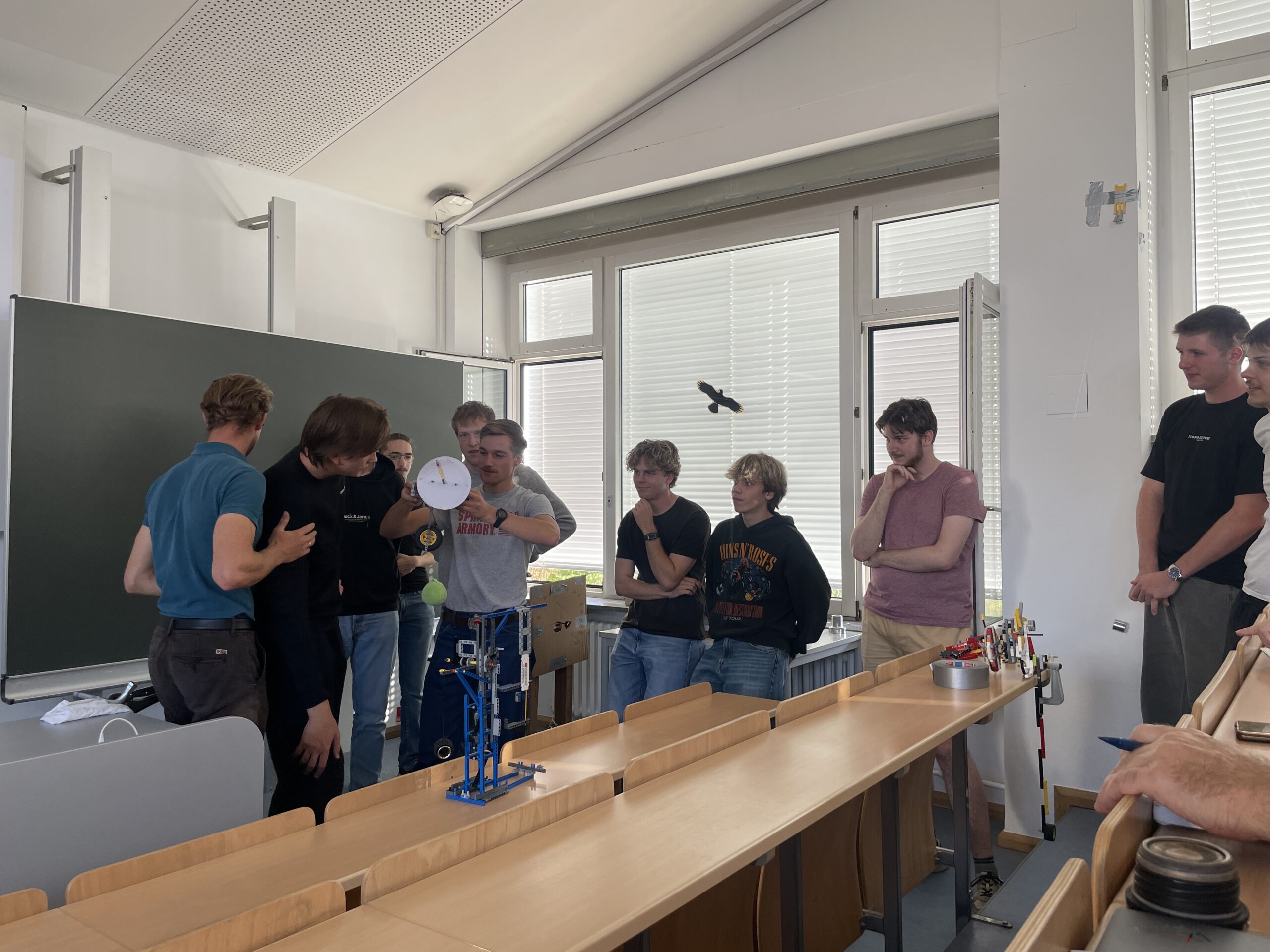 MINT-Schüler untersuchen in einem Klassenzimmer einen kleinen Roboter und ein Papiermodell eines Zifferblatts. at Hochschule Coburg